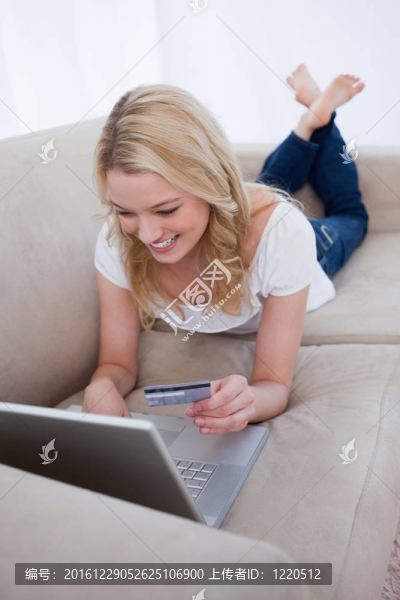 一個面帶微笑的女人在筆記本上打字，手里拿著一張銀行卡