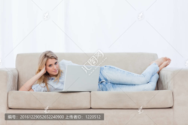 一個(gè)女人看著相機(jī)躺在沙發(fā)上用她的筆記本
