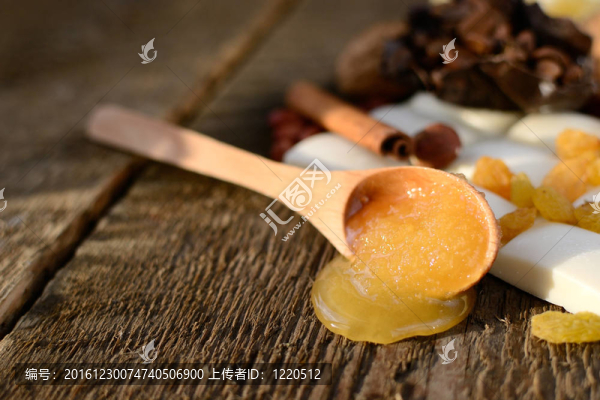 木制的勺子和蜂蜜在一個木桌旁邊的白巧克力；葡萄干；肉桂棒