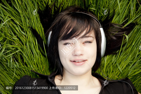 黑發(fā)女孩在綠色的草地上聽音樂。