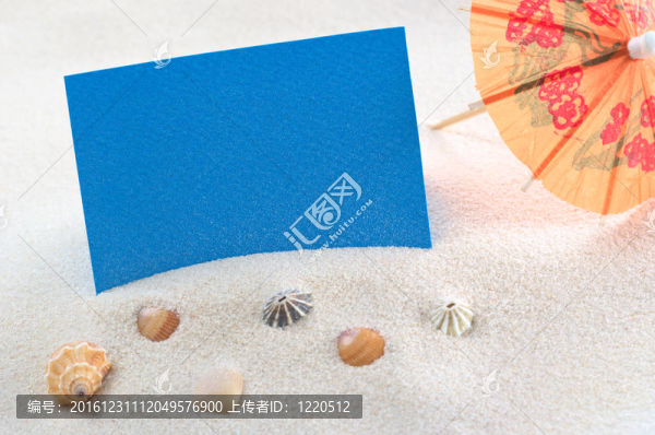 空白的藍(lán)色卡片，橙色的紙傘在沙子和貝殼上（選擇性的焦點；卡片上的焦點）