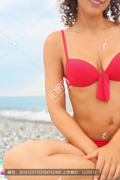 美女身上穿泳裝。她坐在海邊的水邊。