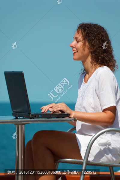 微笑女孩與筆記本電腦。坐在海灘上的桌子上；溫暖晴朗的日子。垂直格式。