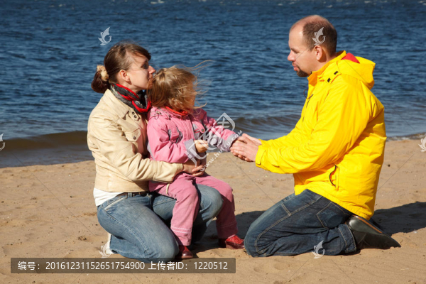 在海灘上和父母在一起的小女孩；晴朗的秋日。父親握著女兒的手。
