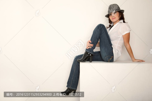 穿牛仔褲的女孩；帽子和白襯衫坐在白色的工作室。橫向格式。