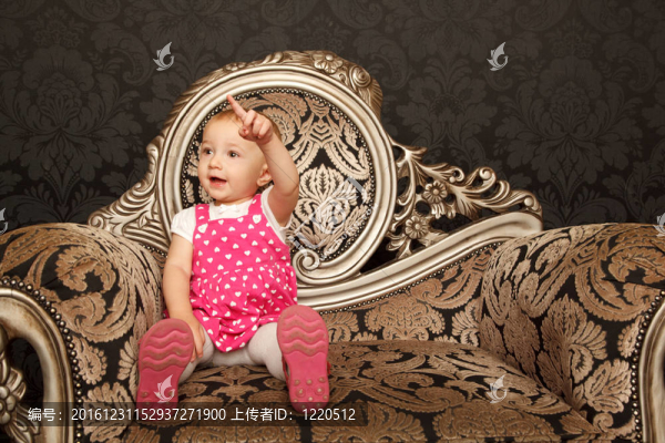 穿著紅色衣服的小女孩坐在扶手椅上，手指朝上。