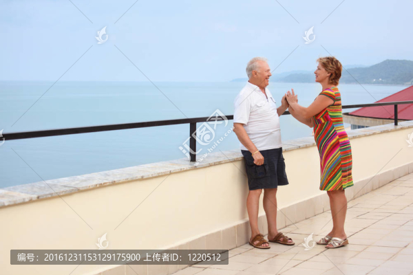 老人微笑著的已婚夫婦在陽臺靠近海岸；扮演情侶