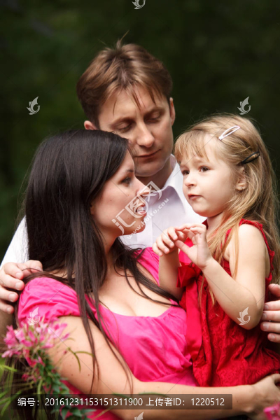 夏日花園中的年輕家庭。媽媽抱著女兒。男人擁抱他們。