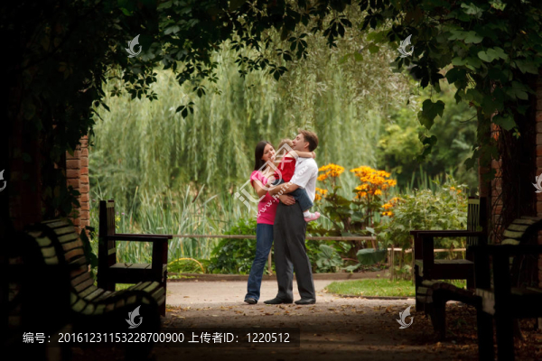夏季植物園中的父母與小女孩。男人抱著女孩。橫向格式。