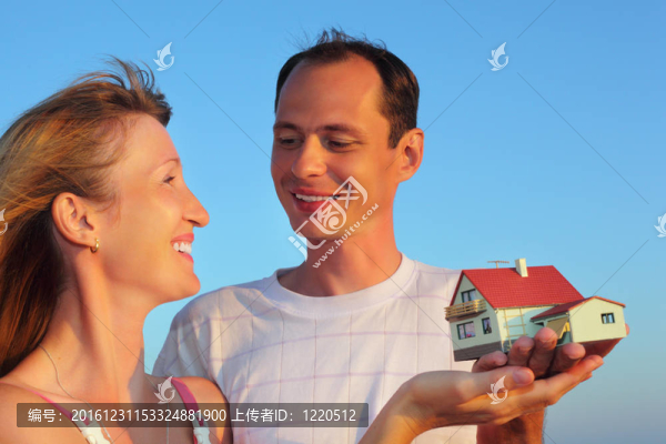 年輕女人和男人手牽手的房子模型與車庫(kù)在天空中的夏天