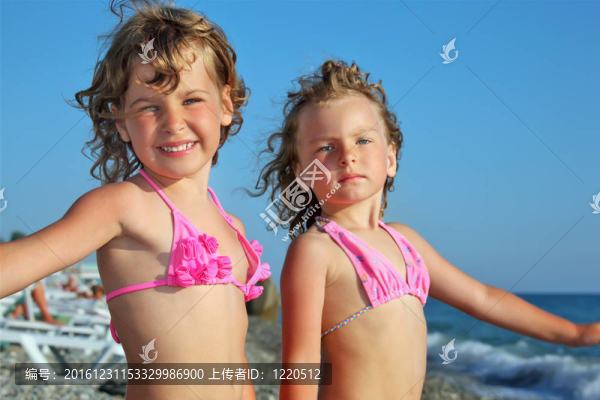 海邊的海灘上兩個(gè)漂亮的小女孩；雙手放在一邊