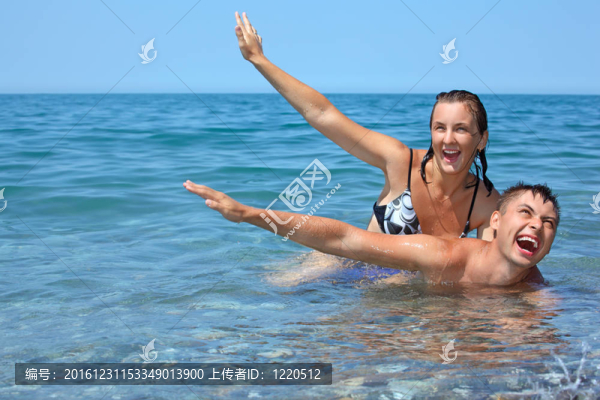 年輕的女人坐在男人的海海岸附近；舉起雙手向上