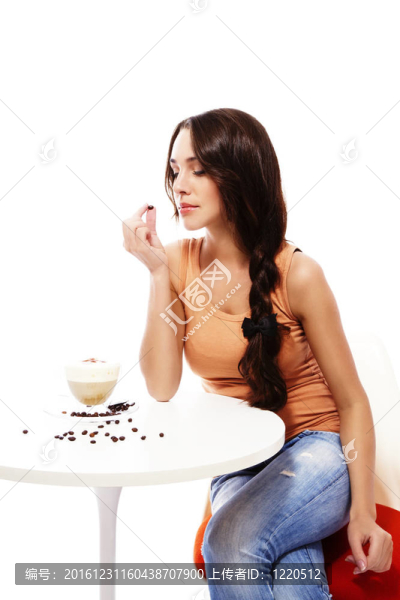 美麗的女人看著咖啡豆在她的手，坐在桌上卡布奇諾咖啡在白色背景