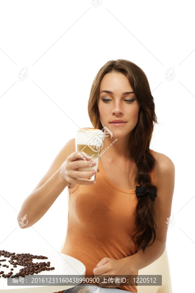 美麗的女人坐在桌旁看著拿鐵咖啡在她手上的白色背景