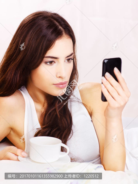 女人打電話，在床上抱著一杯咖啡