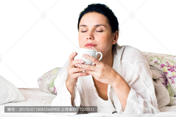 一個(gè)年輕的女人在床上在床上抱著一杯咖啡
