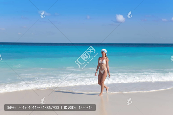 戴著圣誕老人帽子的年輕女子走在海邊的海灘上