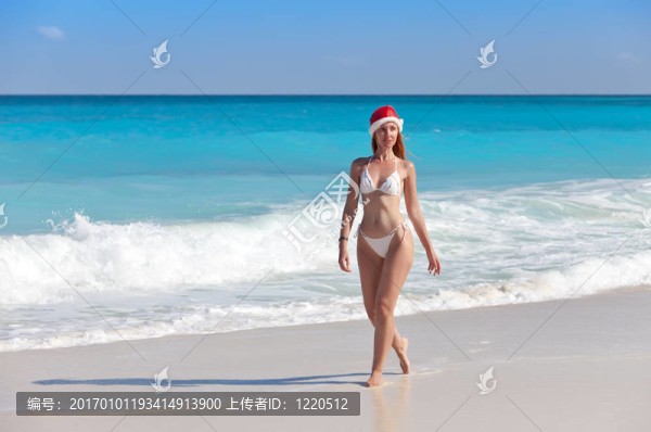 戴著圣誕老人帽子的年輕女子走在海邊的海灘上
