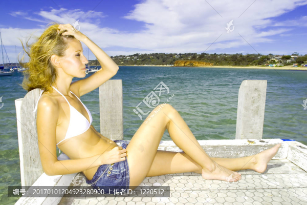一個(gè)年輕漂亮的女人躺在白色的比基尼水邊的頭像照片。