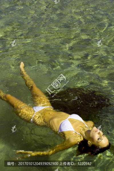 一個(gè)年輕漂亮的女人在一個(gè)白色的比基尼浮在水中放松股票照片。