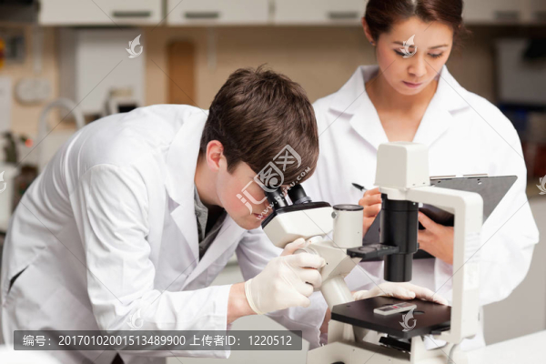 科學(xué)家在顯微鏡下觀察，而他的同事正在實驗室里做筆記
