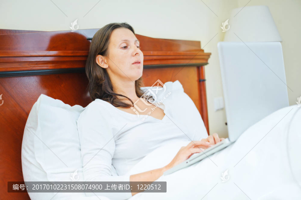 微笑的女人坐在床上使用筆記本電腦