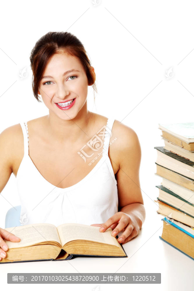 微笑女孩坐在堆的書附近。