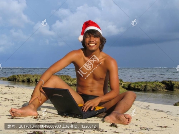 亞洲圣誕老人在沙灘上的筆記本電腦