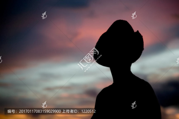 在一頂牛仔帽映襯落日的天空的女人。