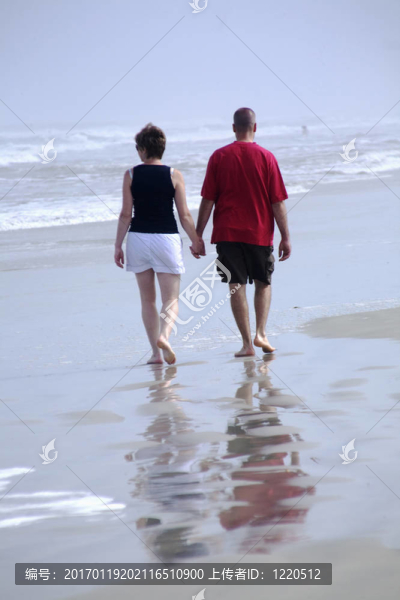 夫婦手牽手，因為他們走在沙灘上濕砂