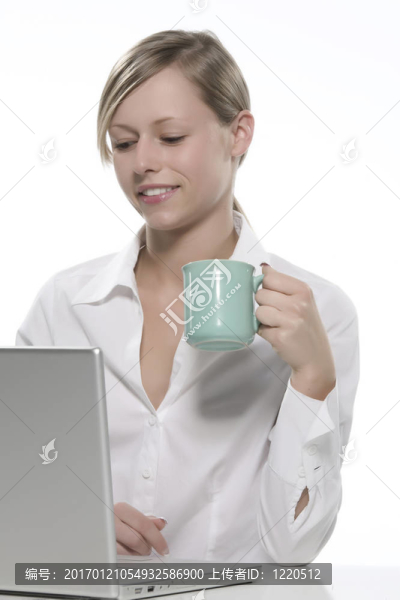 年輕女人看著她的筆記本電腦，喝著咖啡。