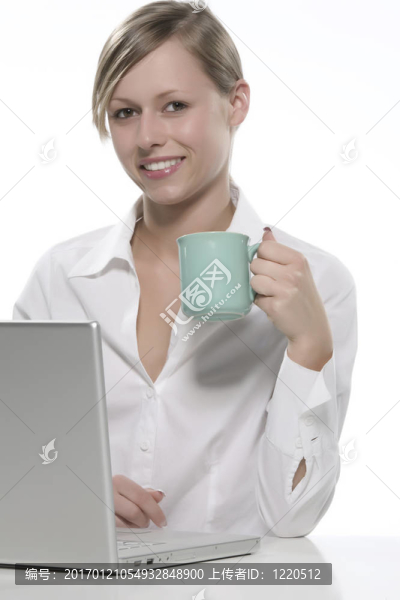 年輕女人看著她的筆記本電腦，喝著咖啡。