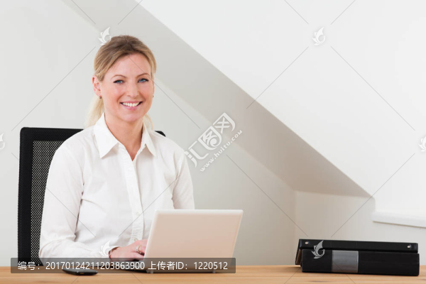 面帶微笑的商務(wù)女性坐在桌上筆記本電腦
