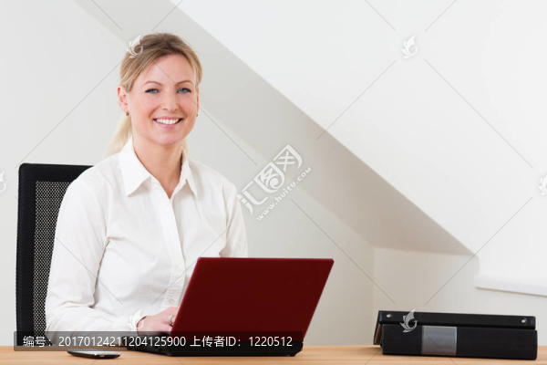 坐在辦公桌上的商務(wù)女性用紅色筆記本電腦