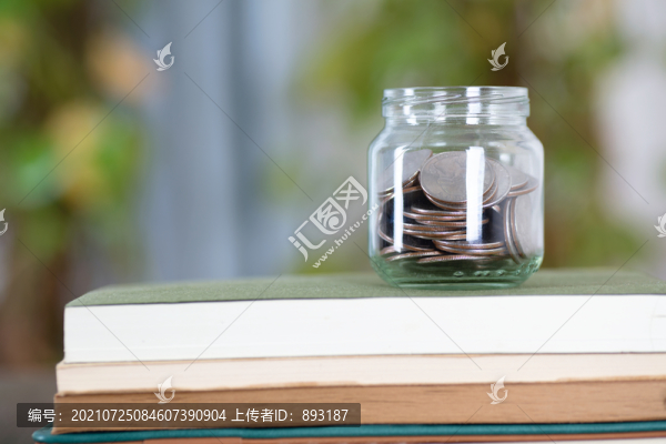 一摞書上的玻璃存錢罐