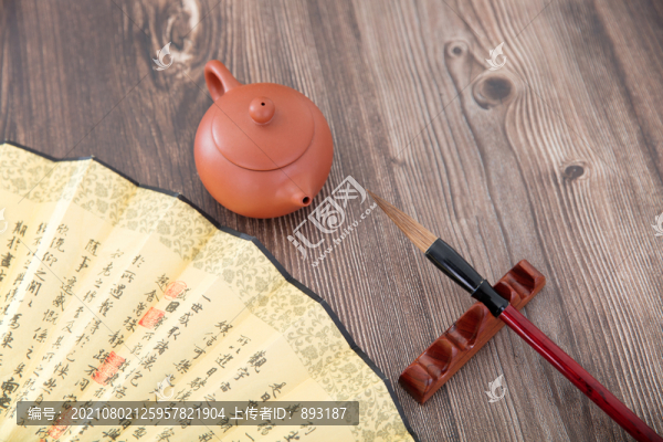 書桌上的毛筆和紫砂壺和一把折扇