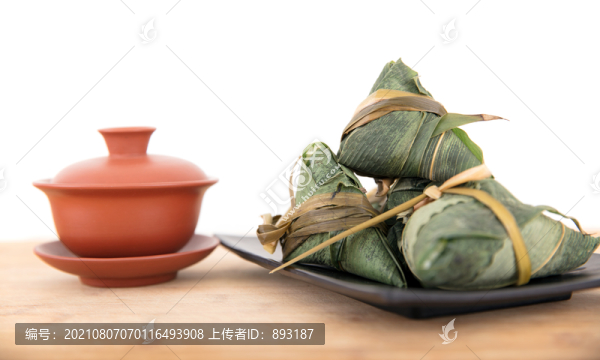 白背景前砧板上一盤粽子和一碗茶