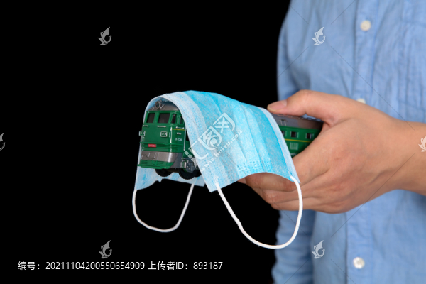 黑背景前手拿被口罩蓋著的火車模