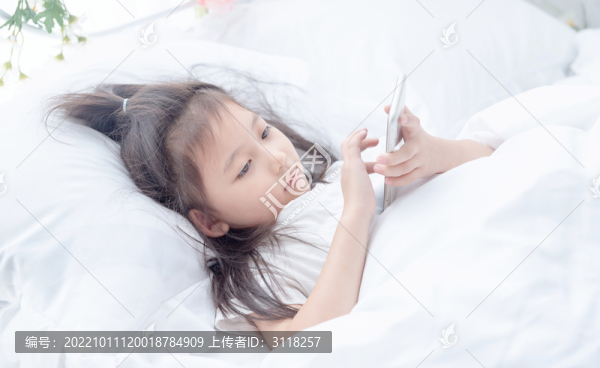 床上使用手機的小女孩