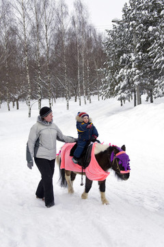 孩子在冬天公园和妈妈一起骑小马