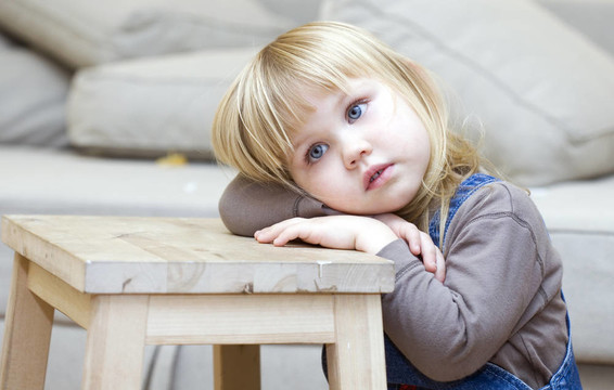 害怕或体贴的金发碧眼的小女孩。坐在地板上；躺在木凳子上