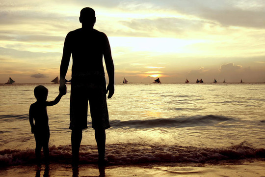 父亲和儿子在日落海面背景的轮廓