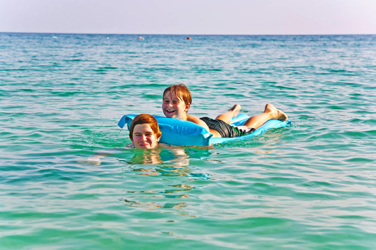 兄弟们一起在一个美丽的大海，在空气中的空气床垫清澈的水和蓝天