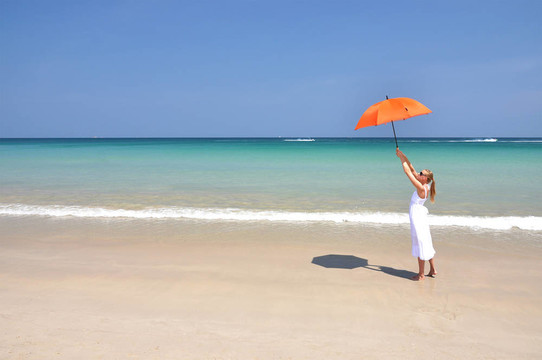 沙滩上带着橙色雨伞的女孩