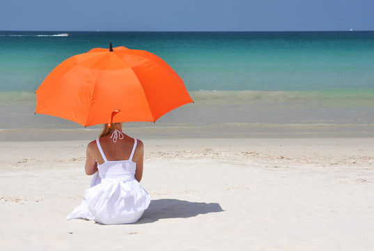 沙滩上带着橙色雨伞的女孩