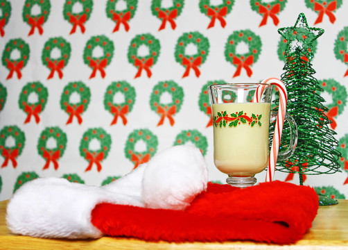 一杯圣诞蛋酒在桌上用花环的背景和Santa帽和圣诞树，使用选择性聚焦和浅景深