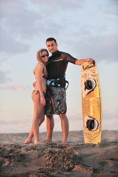 在日落时在海滩上摆姿势的冲浪夫妇