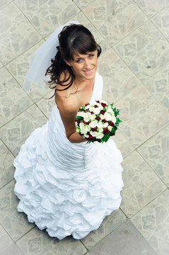 穿着白色连衣裙的苗条新娘带着花束向上看