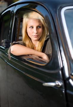 美丽的年轻金发女孩在黑色老爷车。