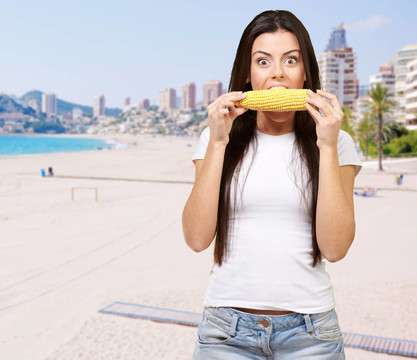 年轻女子吃玉米棒对海滩写真